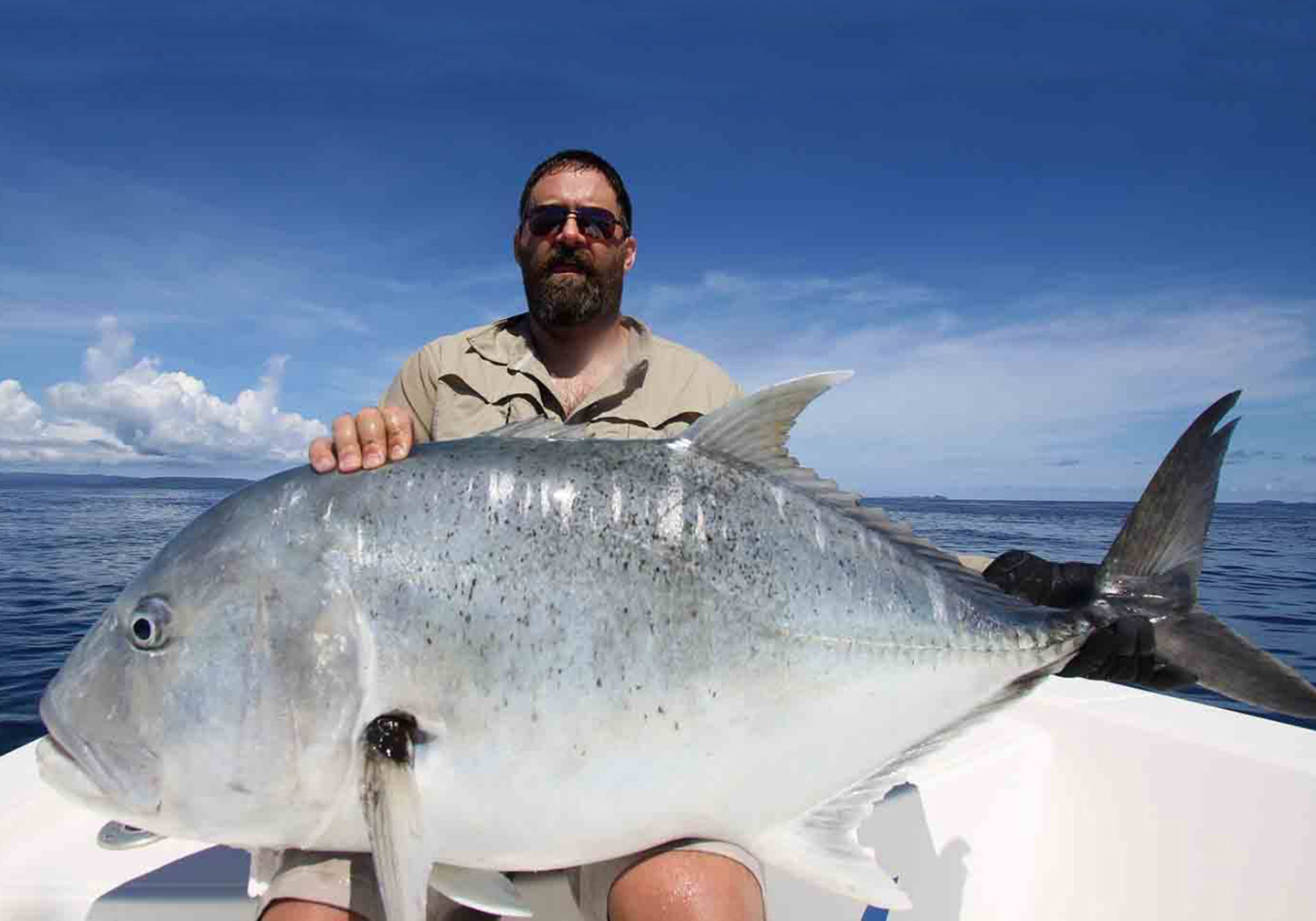 Ein m&auml;nnlicher Angler mit einer gro&szlig;en Dickkopf-Stachelmakrele auf seinem Scho&szlig;.