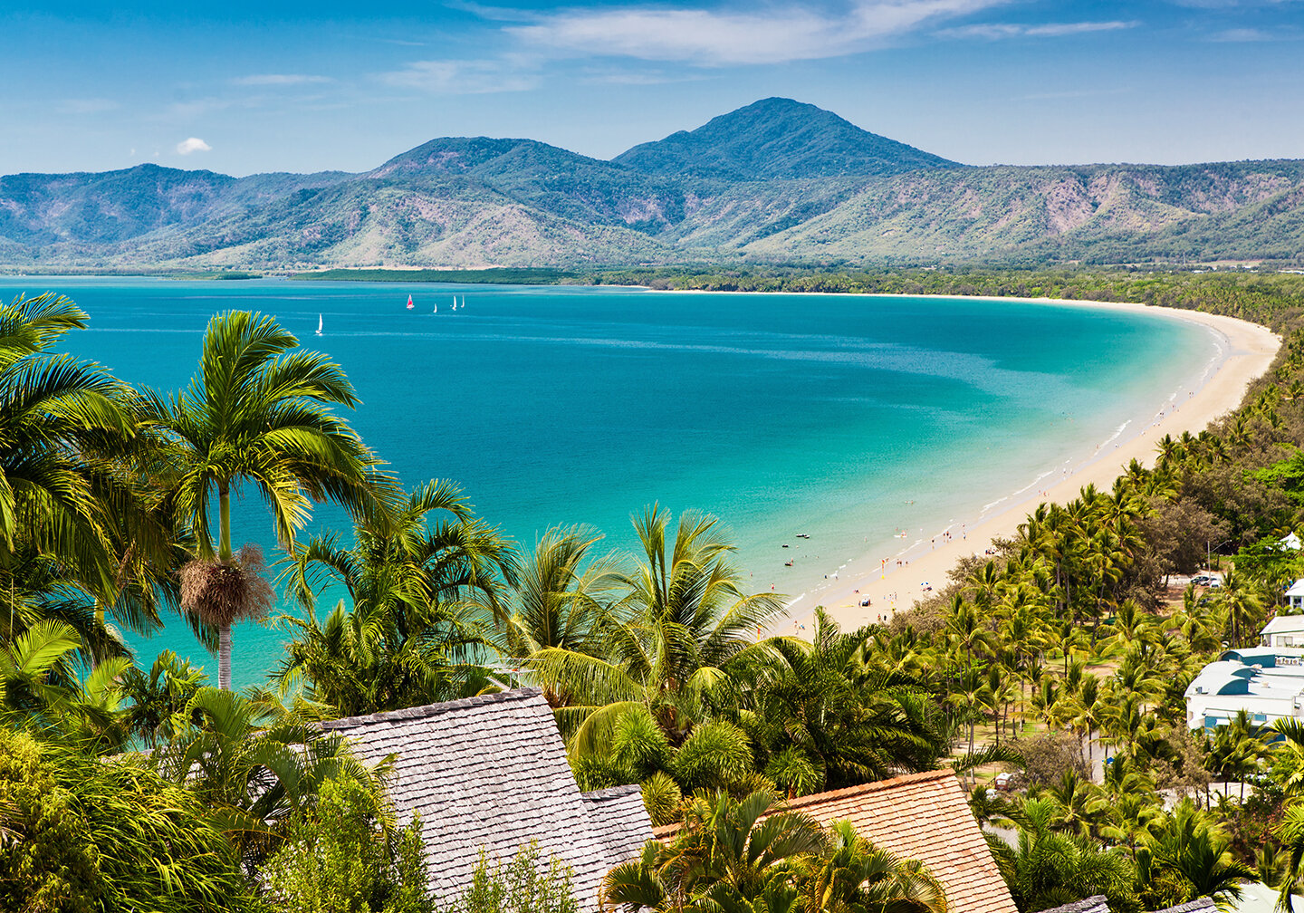 Ein Blick auf die Bucht in Cairns, Australien, mit gr&uuml;nen B&auml;umen, wei&szlig;em Sand und t&uuml;rkisfarbenem Wasser.