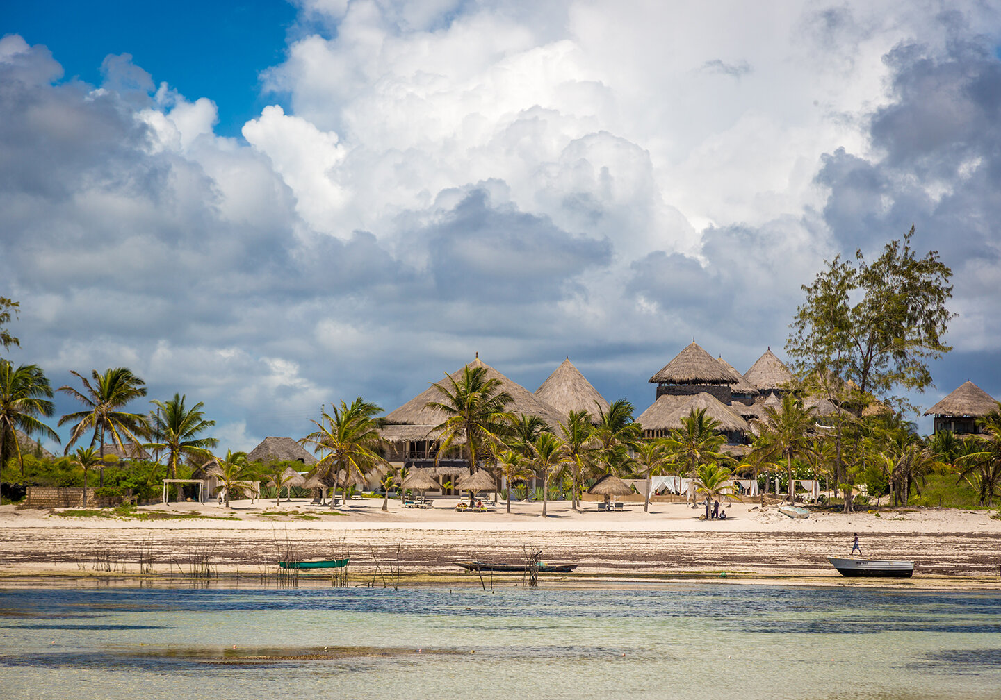 Ein Blick vom Meer auf die traditionellen H&uuml;tten in Watamu, Kenia. Im Vordergrund steht flaches, klares Wasser und in der Ferne bew&ouml;lkter Himmel.