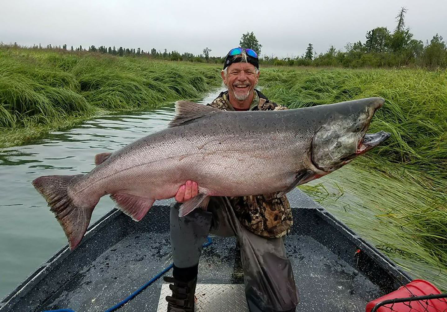 Ein gl&uuml;cklicher Angler auf einem Boot, der auf einer Angeltour am Kenai in Alaska einen gro&szlig;en K&ouml;nigslachs h&auml;lt.