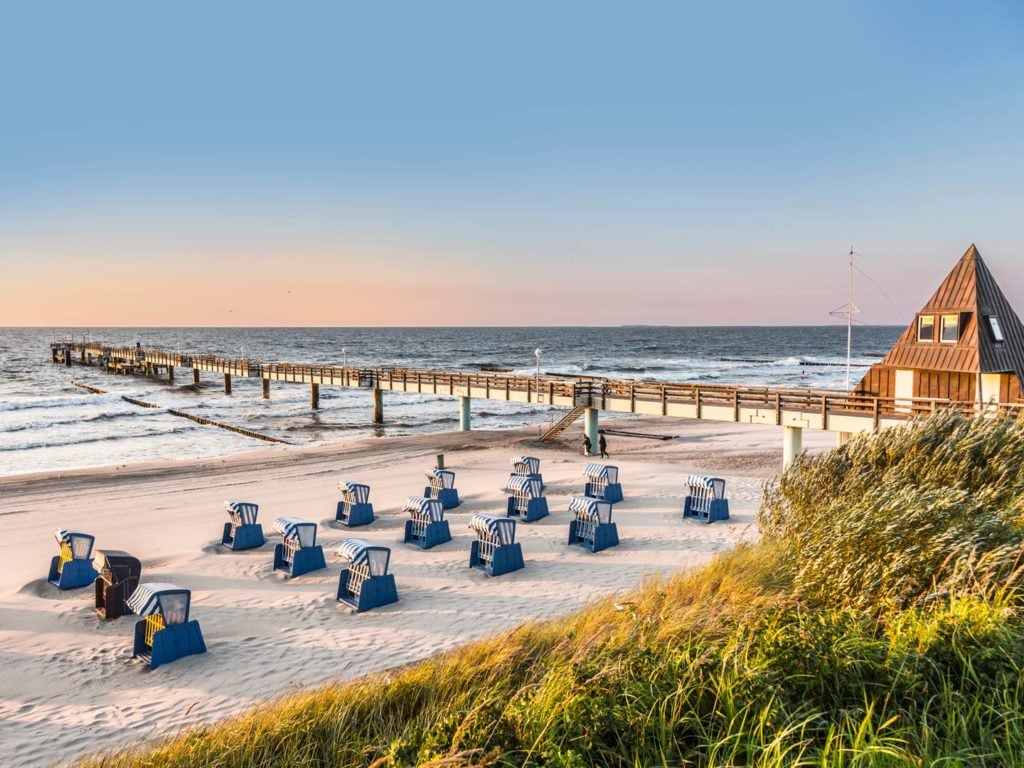 Ein Ostseestrand mit Blick auf einen Angelsteg in der Morgensonne.