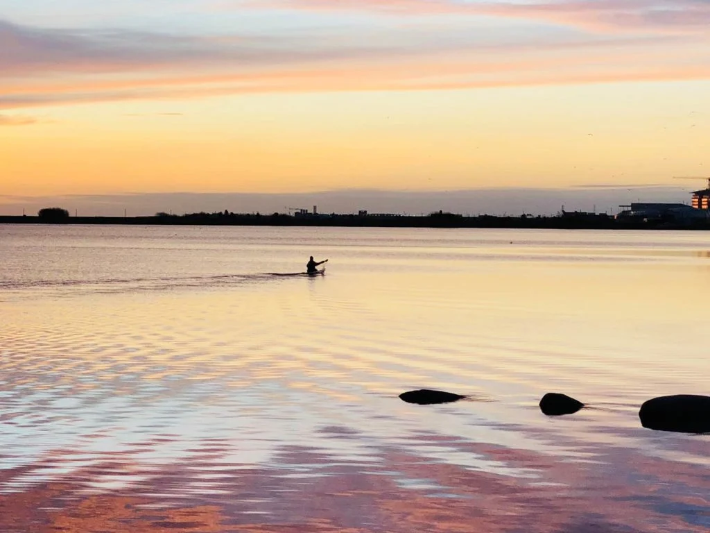 Ein Angler, der bei Sonnenaufgang von Kopenhagen aus auf der Ostsee Kajak f&auml;hrt.