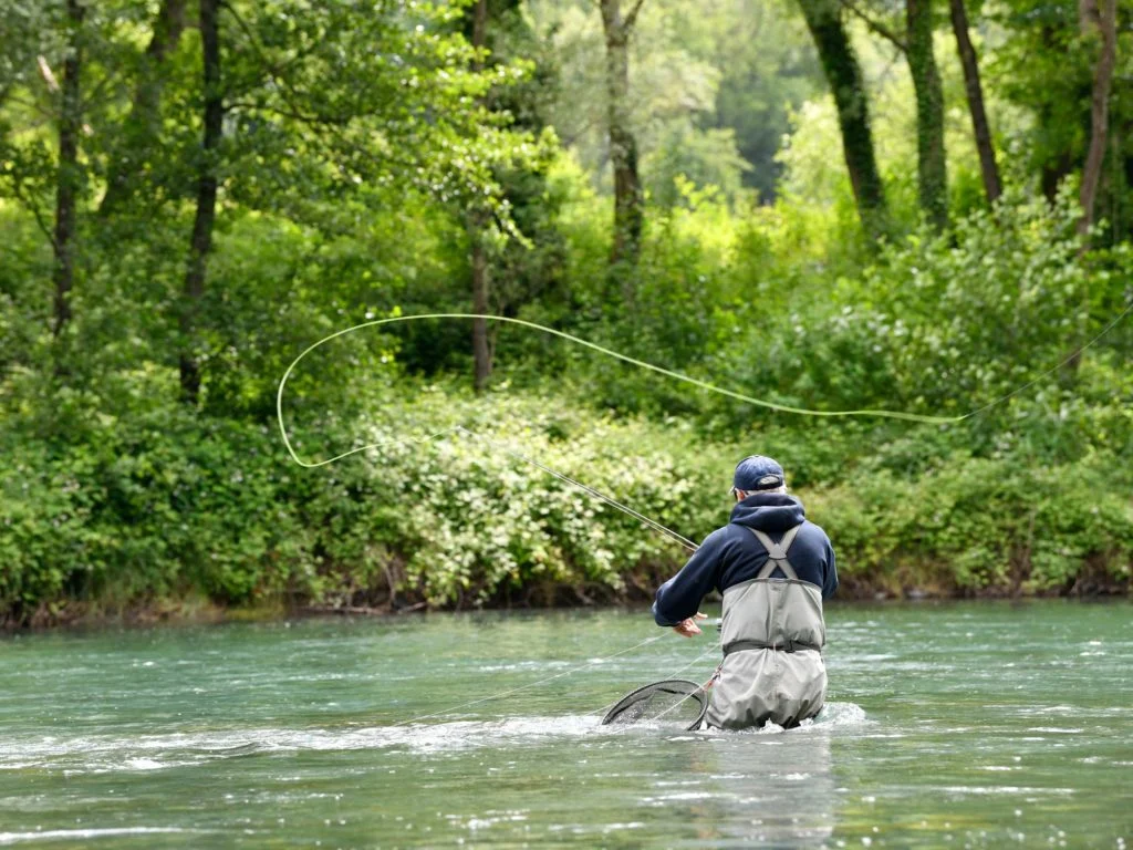 Ein Fliegenfischer, der in einem Fluss steht und seine Angel auswirft.