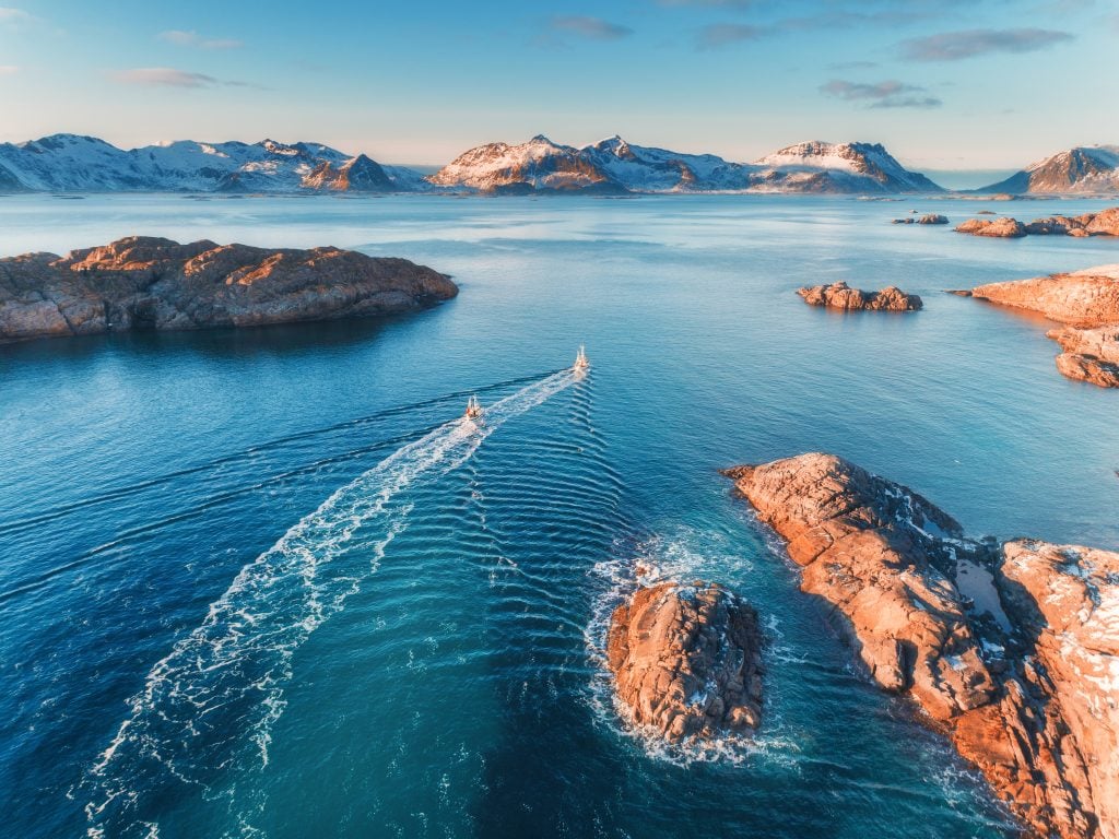 An aerial view of a fjord in Norway with small islands visible in the nearground and tall mountains in the distance.