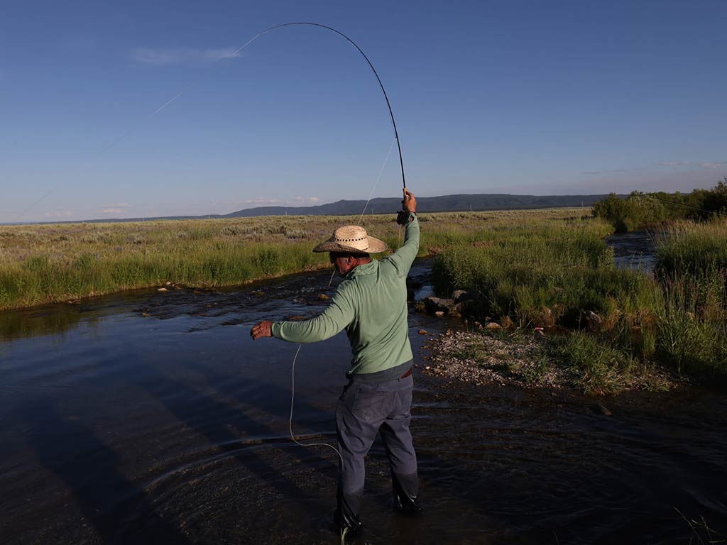 A view from behind of a man fly fishing in a river in Wyoming during summer.
