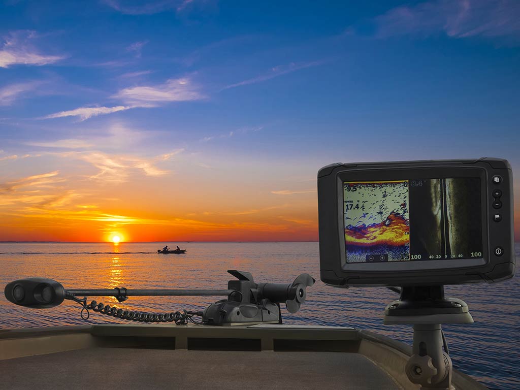 A fishfnder screen with forward-facing sonar displays underwater data on a boat at sunset, while a small boat floats in the distance.