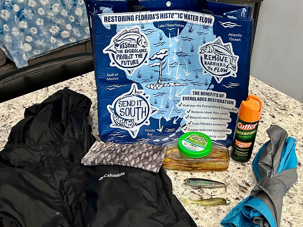A gathering of some essential outdoor gear on a bead, featuring a black jacket and a patterned neck gaiter for sun and bug protection.