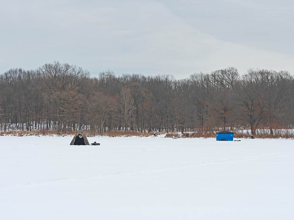 Two small tents stand on a snow-covered field in Illinois, showing off-season camping or ice fishing with leafless trees and a cloudy sky behind.