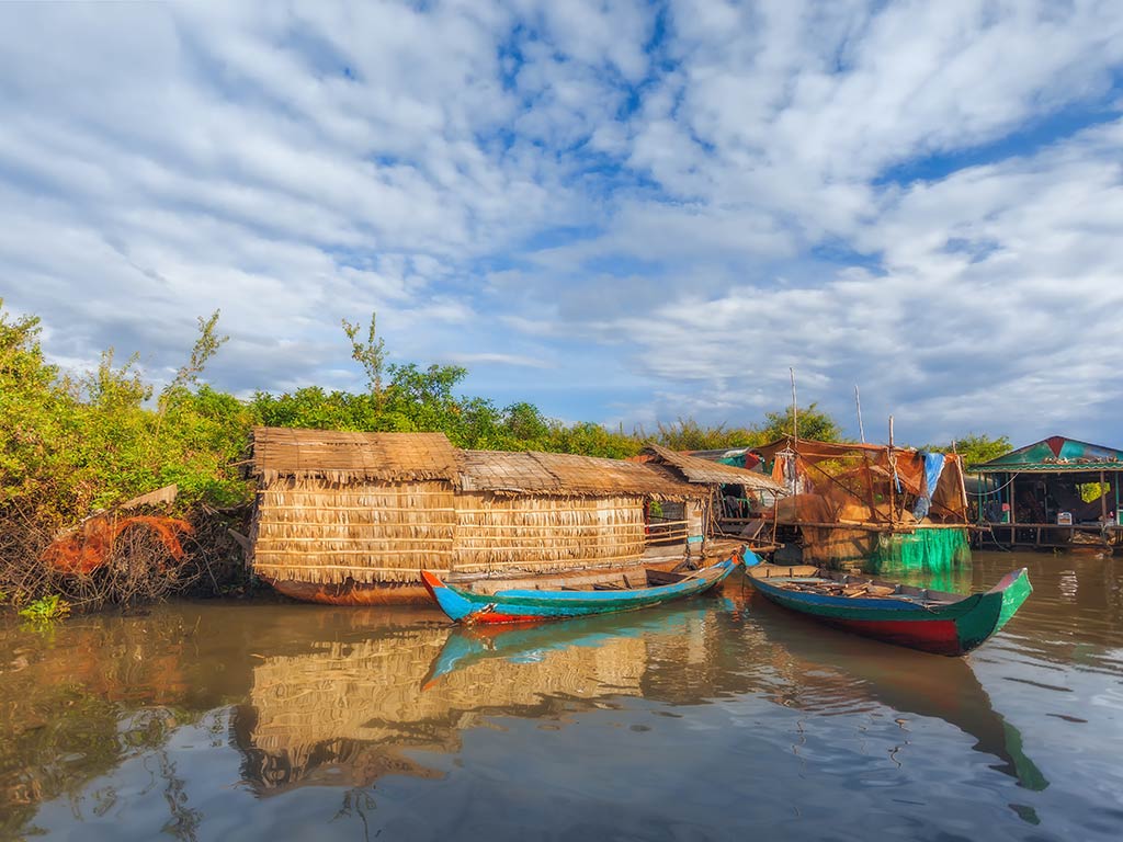 A view across the water towards a traditional southeastern Asian fishing boat and a riverside hut on a bright day.