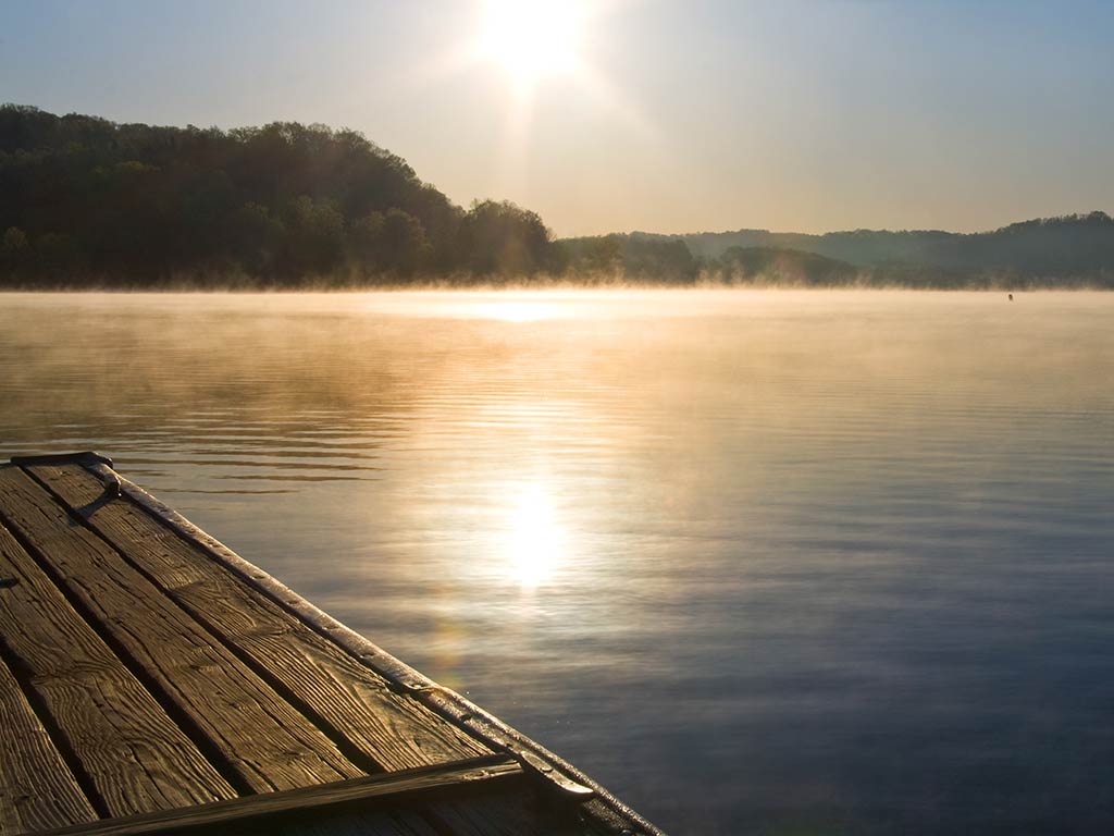 A view across the calm waters of Melton Lake on the Clinch River in Tennessee in the early morning, as the rising sun shines off the water.