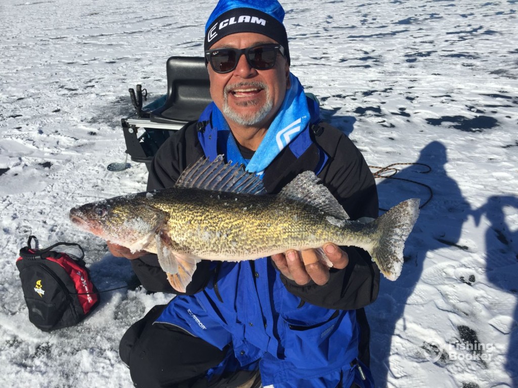 A man in winter clothing holds a large Walleye while sitting on a snowy, frozen lake, embracing the thrill of fishing in Colorado.