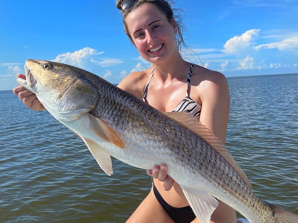 A closeup of a woman holding a large Redfish while on a boat on a clear day.