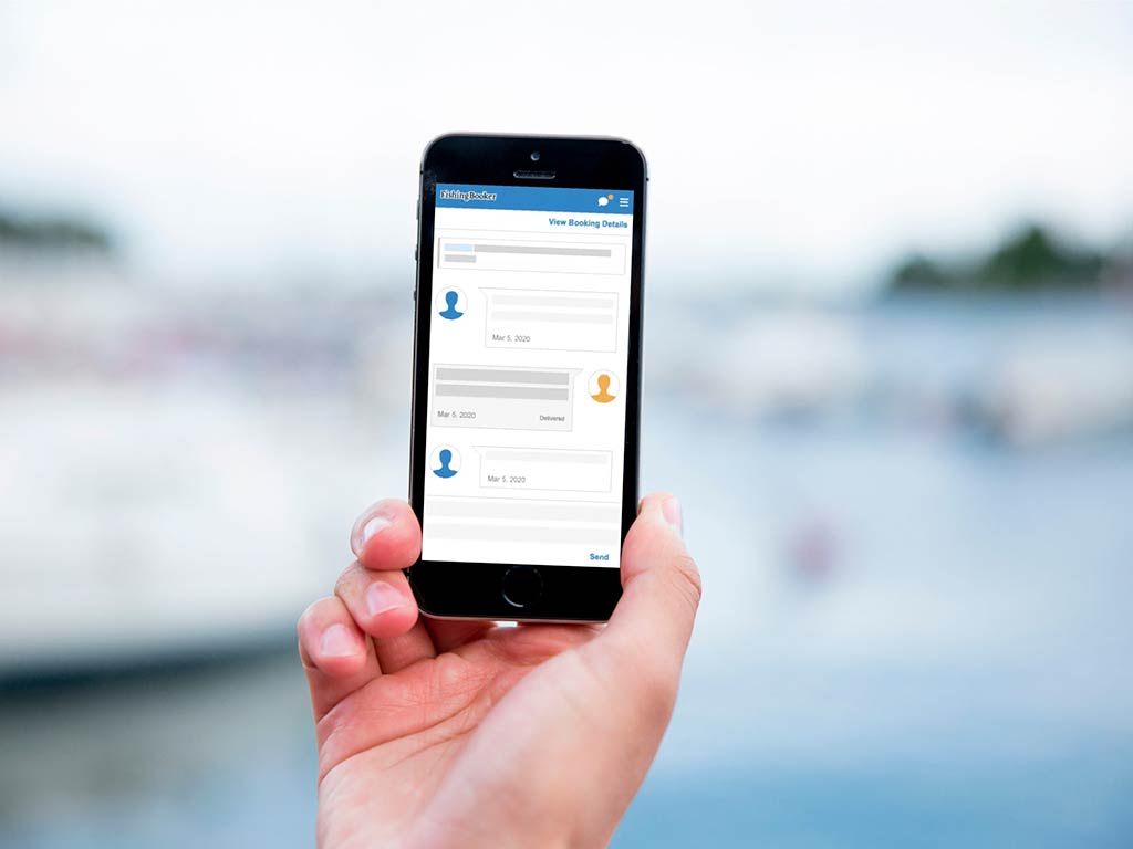 Рука держит мобильный телефон с отображением инструмента мгновенных сообщений FishingBooker на фоне размытой марины.