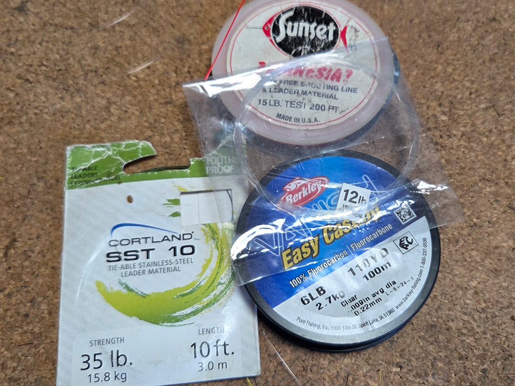 A closeup of fishing leader materials, mostly in their packaging, laid out on a table.