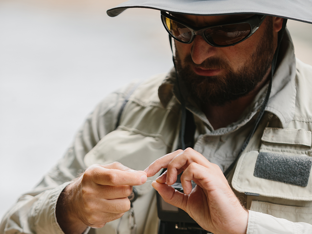 A man in sunglasses concentrates as he ties something onto his fishing line