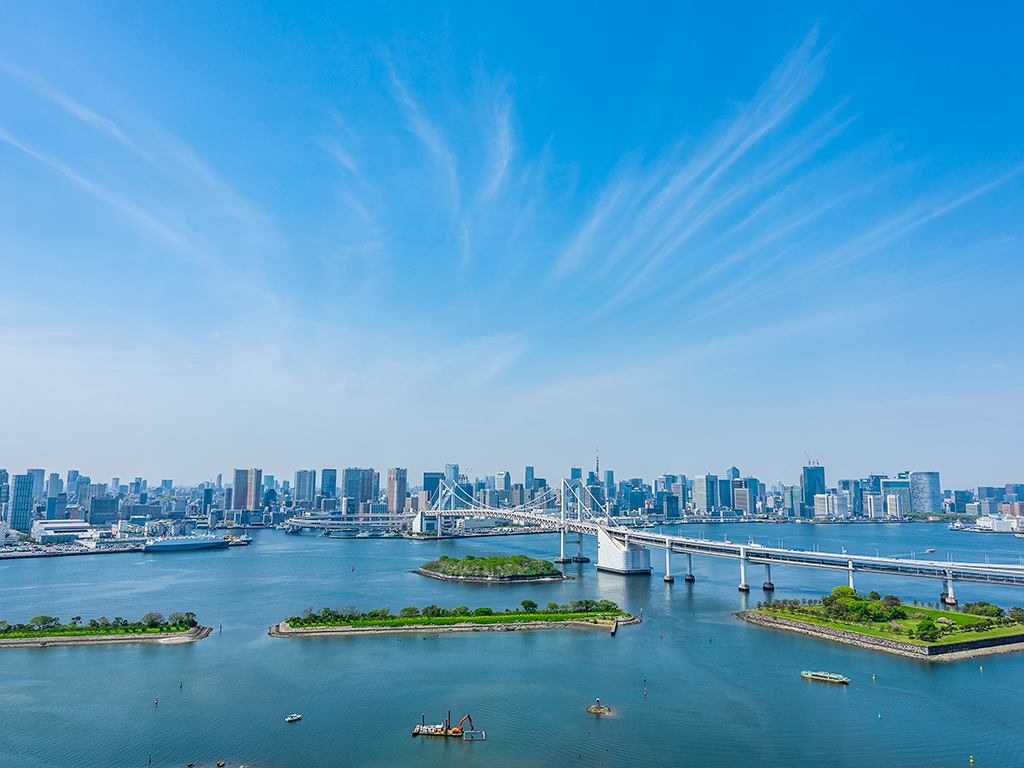 A view across the open waters of Tokyo Bay towards the city's skyline on a clear day, with islands and boats visible in the foreground.