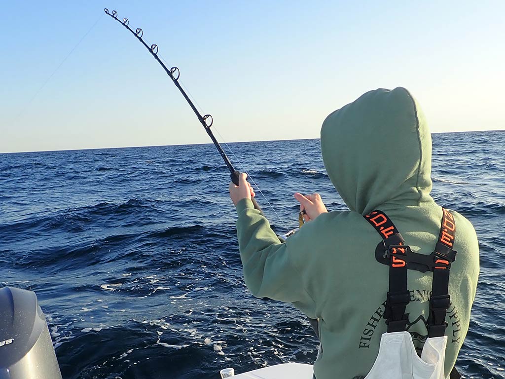 A view from behind of an angler on a boat, casting a heavy-duty fishing rod for Tuna on the open seas.