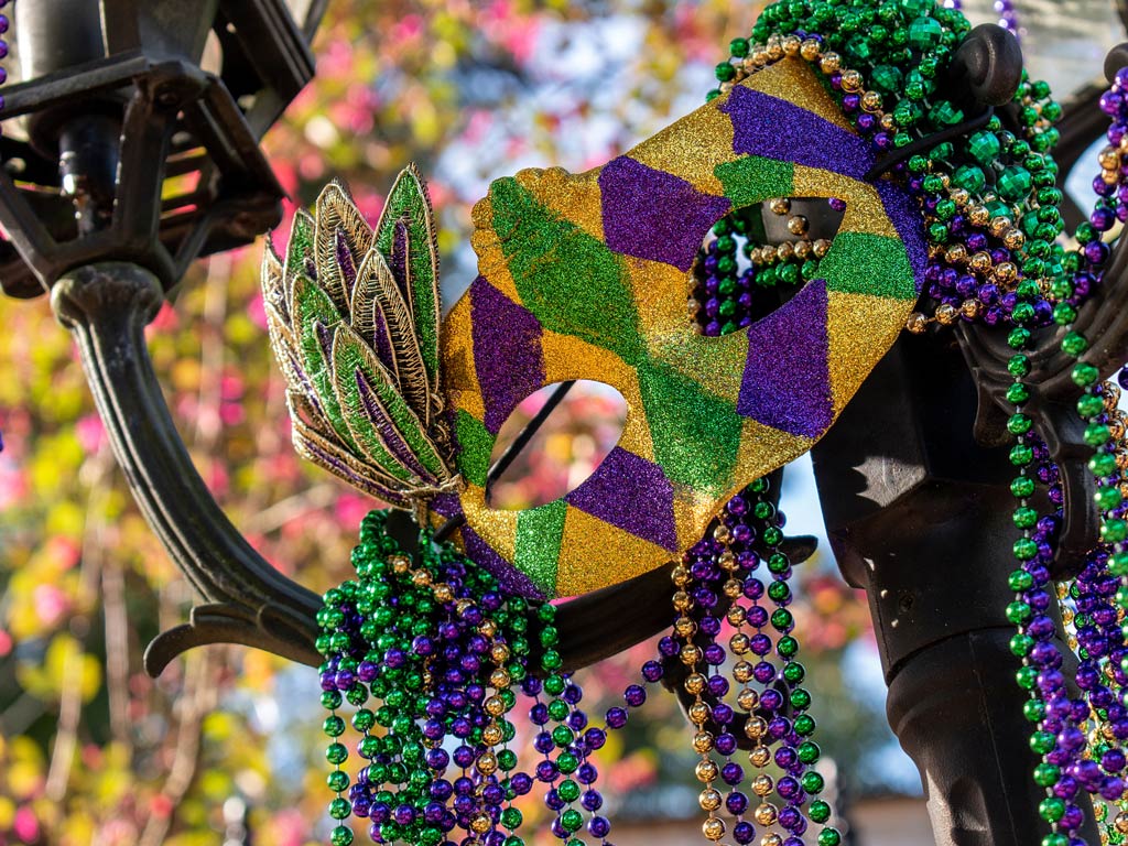 A Mardi Gras mask in purple, green, and gold's resting on a lamp post, surrounded by colorful bead necklaces in Mobile, Alabama during winter.