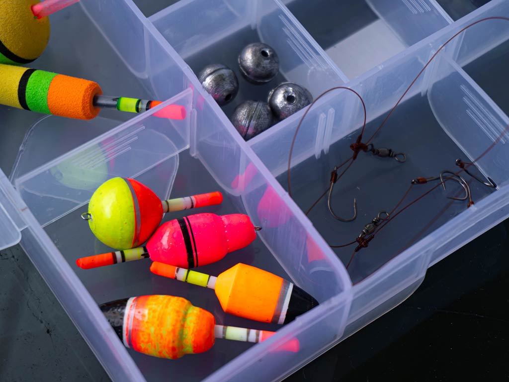 A plastic tackle box that's got colorful fishing bobbers, fishing sinkers, and fishing hooks with attached lines.