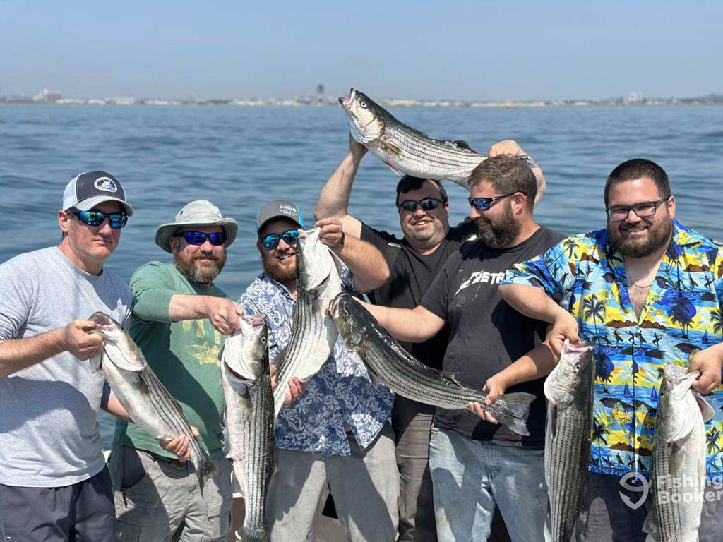 A photo featuring six friends standing on a charter boat and happily posing with a fish or two each on a Boston fishing trip.