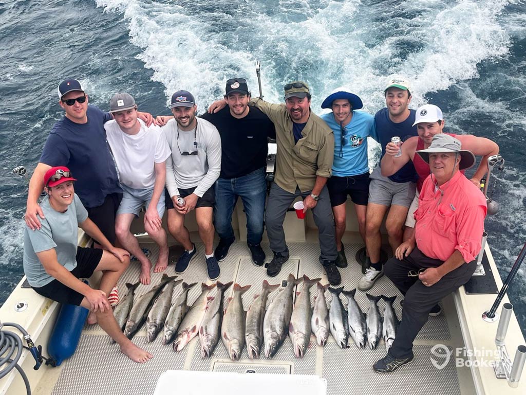 A large group of anglers posing on a charter boat with the fish they caught on a Chicago fishing trip placed in front of them on the boat’s floor.