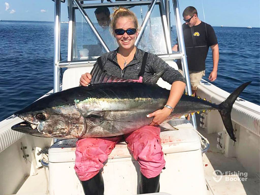 A woman smiles as she sits with a Bluefin Tuna across her lap after on a successful Stellwagen Bank Bluefin fishing trip.