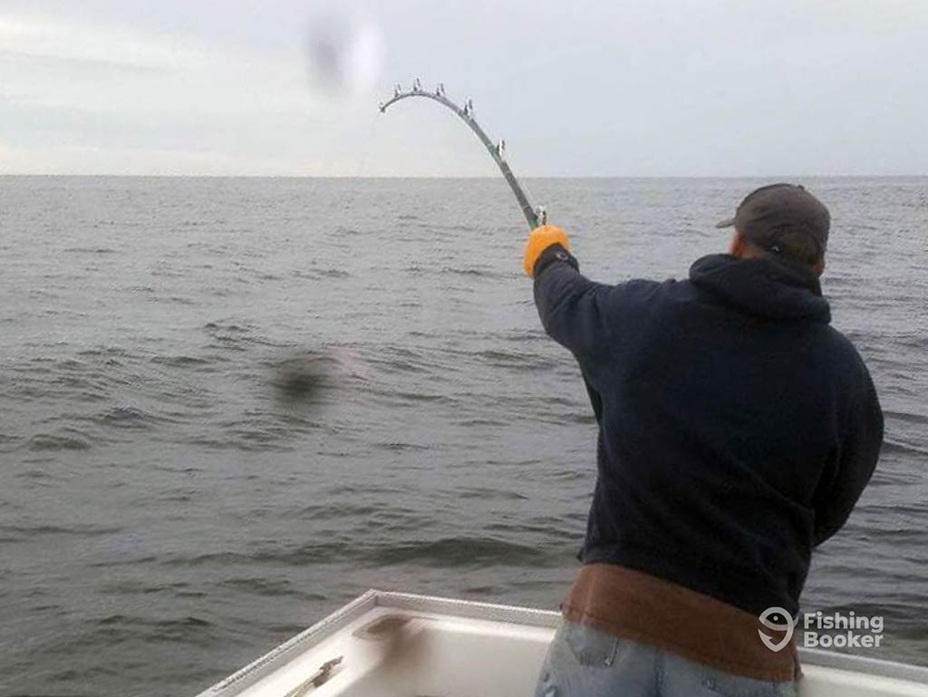 A view from behind of a man battling with a Tuna at the end of his rod offshore near Stellwagen Bank on a rainy day, with a raindrop visible on the image as if on the lens of the camera.