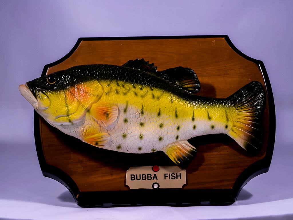 Декоративная игрушка в виде басса, установленная на деревянный пьедестал, как трофейный улов.
