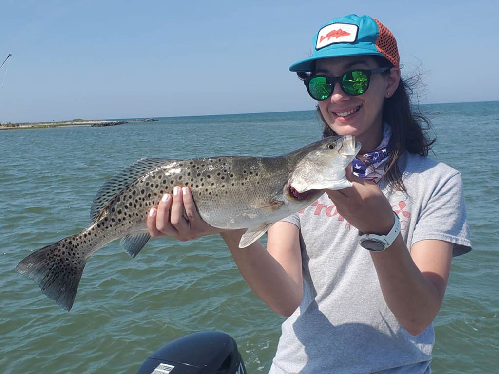 Молодая женщина в бейсболке держит пятнистого фореля на лодке в ясный день.