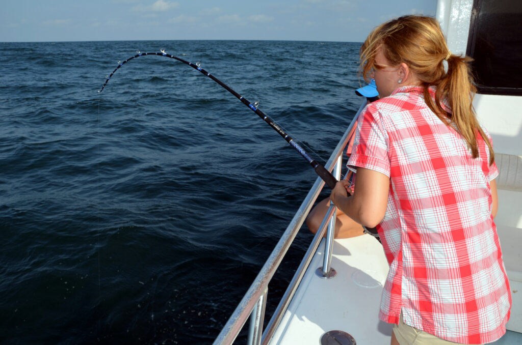 Someone in a red plaid shirt's fishing from a boat, holding a bent fishing rod over the water.