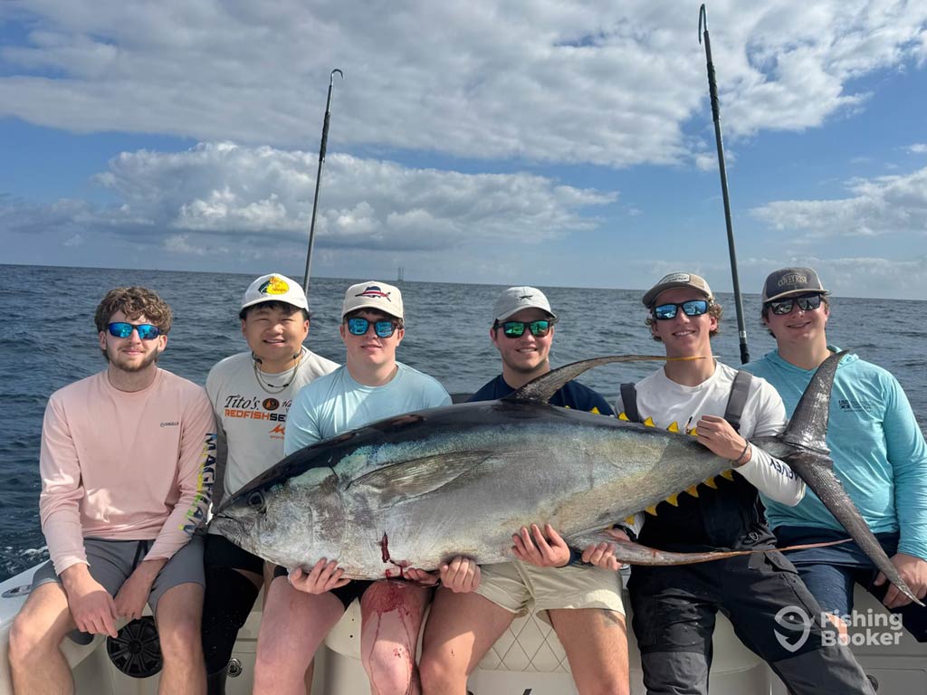 Six young adults and first-time anglers sitting on a charter boat offshore and holding a large Tuna, showing off one of the top Memorial Day fishing catches in Venice, LA with the ocean and rods in the background.