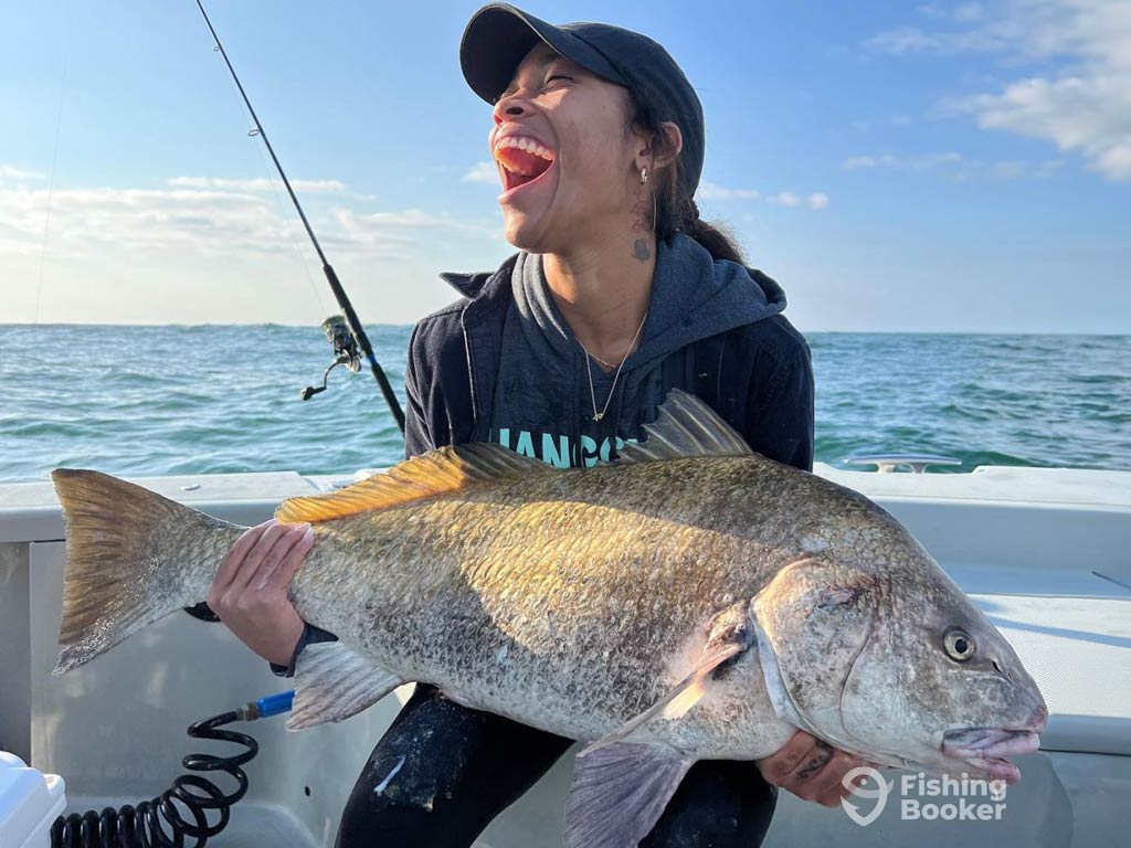 A female angler, sitting on a charter boat, smiling wide while holding a big Redfish, caught while fishing in the South Carolina during spring.