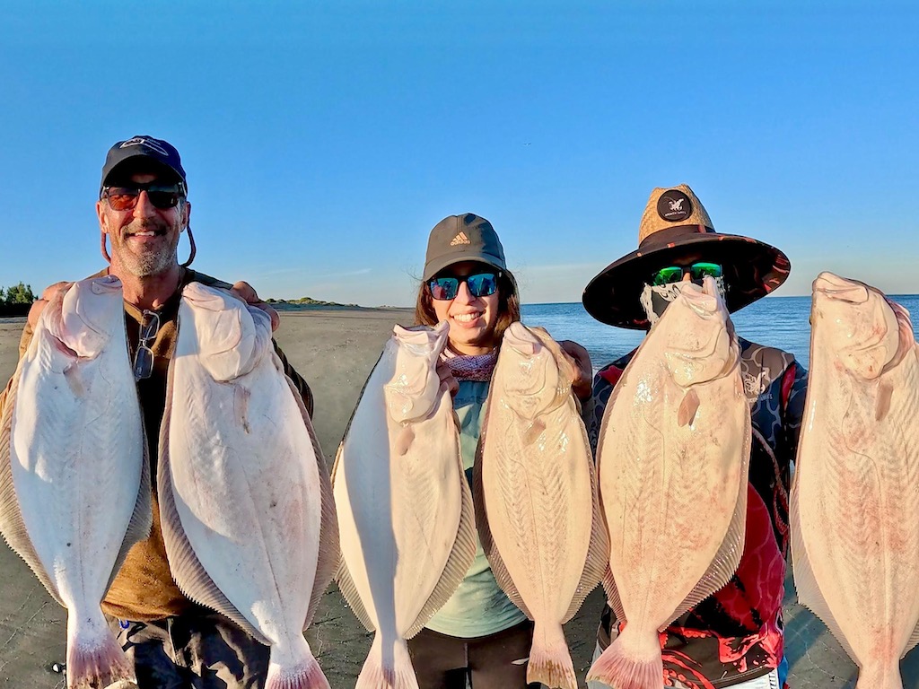 Three men holding up two Halibut each on a fishing trip in Baja California on a clear day.