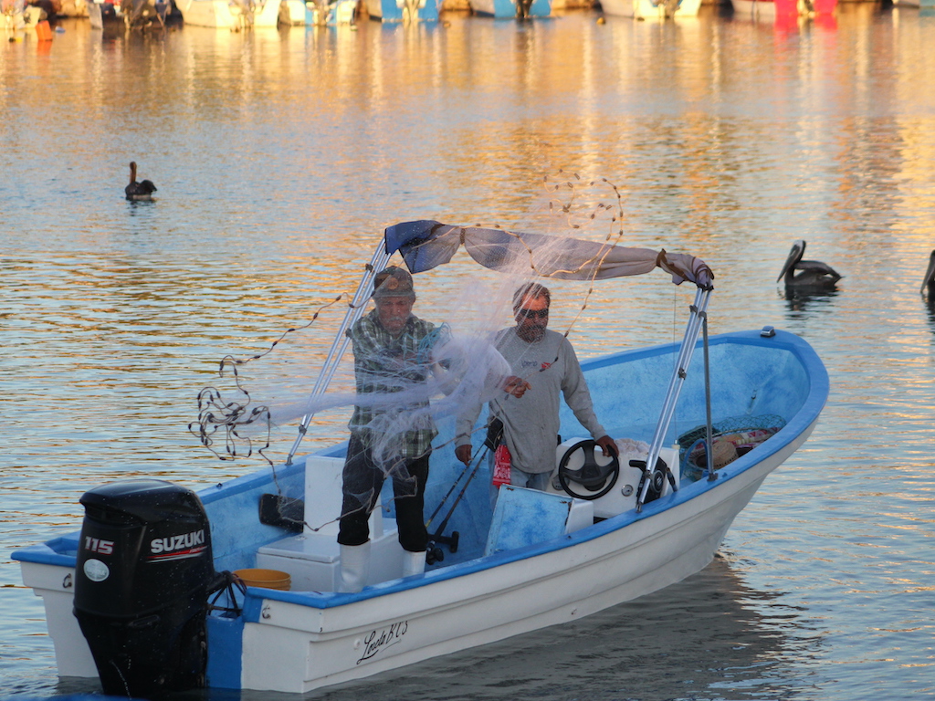 A view of two fishermen on a boat throwing a net into the water at sunset in Mexico.