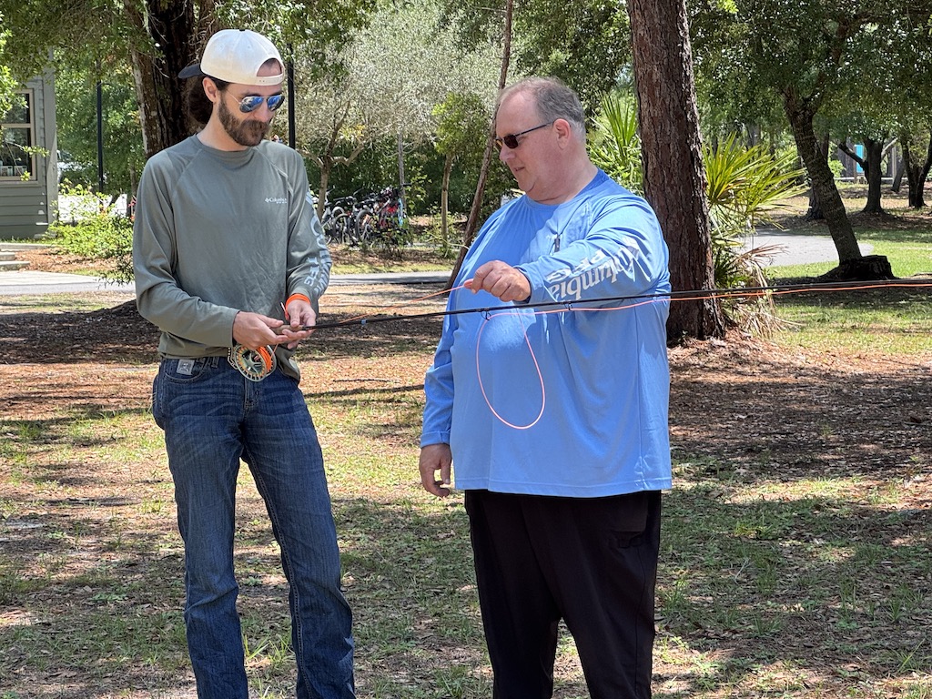 A fishing instructor showing a leaner how to cast a fly fishing line on dry land as part of a fishing event.