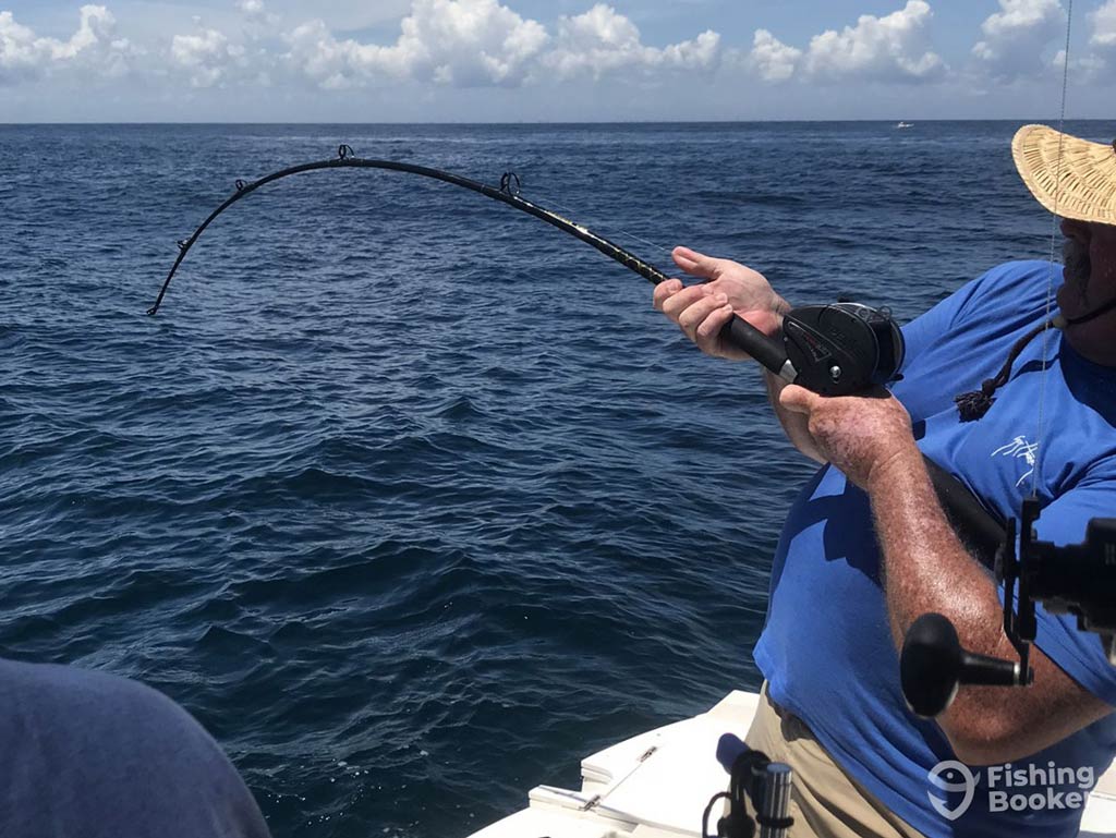 A photo featuring an angler in a blue shirt holding a bent fishing rod on a boat, reeling in their catch over the open ocean—living out that funny fishing saying "Give a Man a Fish, and You Feed Him for a Day. Teach a Man to Fish, and You Feed Him for a Lifetime"