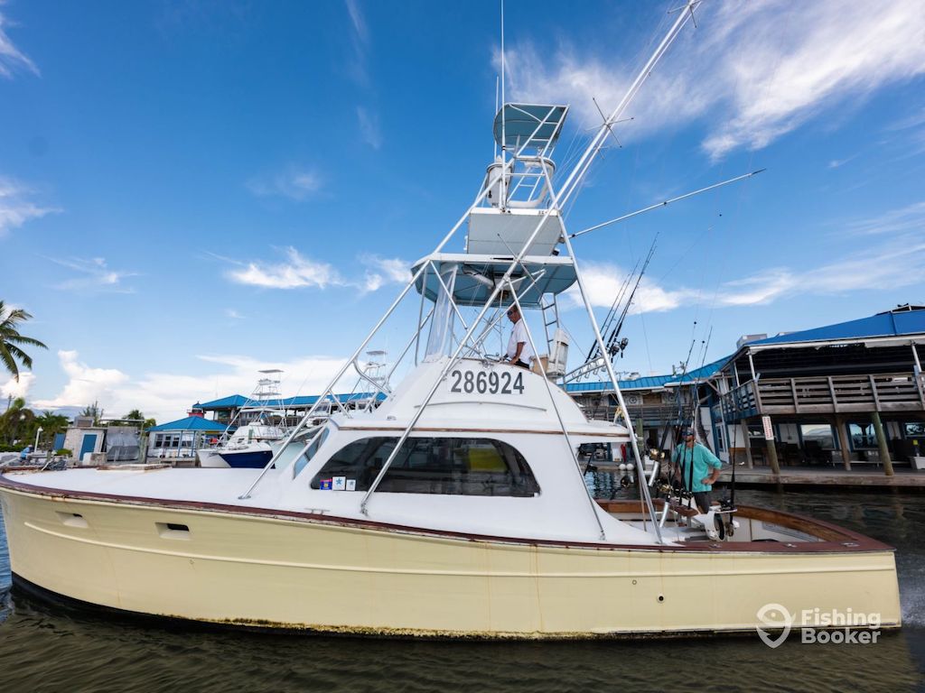 A white fishing boat is docked near a marina, in Islamorada, and there are people on board with fishing rods visible.
