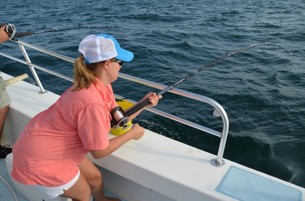 Person in a pink shirt and blue cap's fishing from a boat, holding a rod bent over the side, hoping to hook a big Reef Donkey beneath the waves.