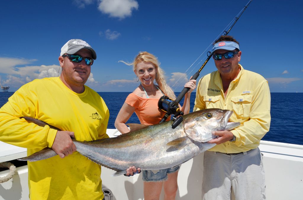 Three people on a boat are holding a large Reef Donkey with fishing gear, set against the ocean and blue sky in the background.