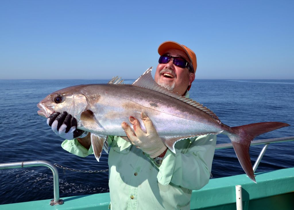 A man’s wearing sunglasses and gloves as he holds a large Reef Donkey on a boat, with the ocean and clear sky behind him.