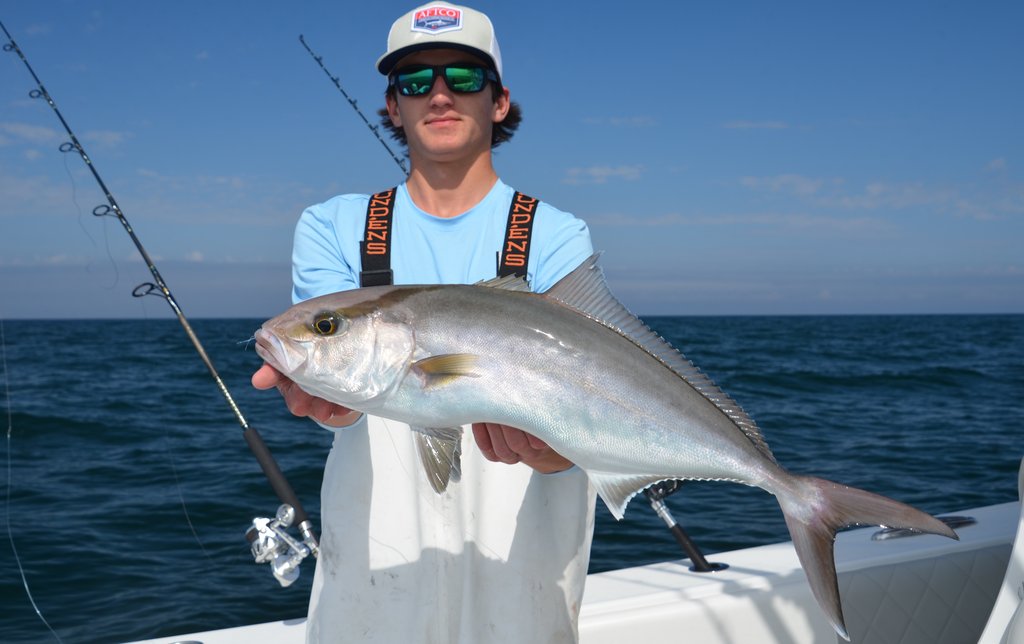 Someone's wearing sunglasses and a hat while holding a big Reef Donkey on a boat, with fishing rods behind them and the ocean stretching out in the background.