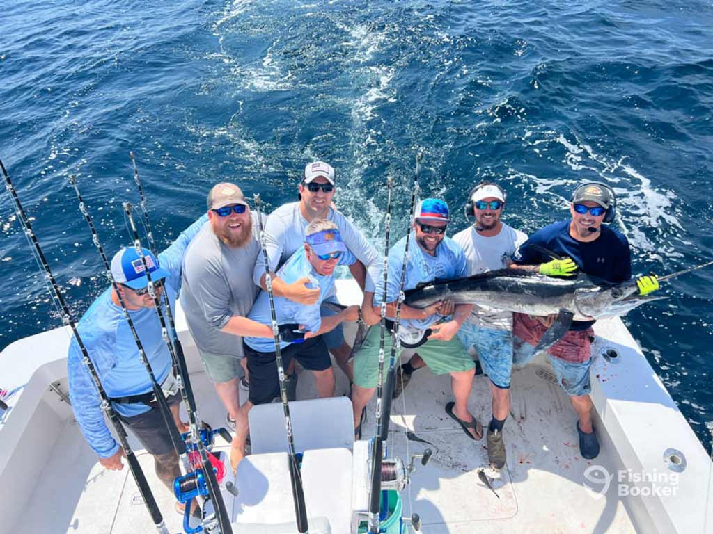 Six deep sea anglers on a charter fishing boat at the White Marlin Open proudly hold a large Marlin, with the ocean and mounted rods in the background for that perfect tournament vibe.