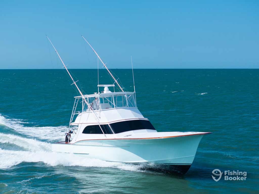 A white sport fishing boat’s cruising on blue water under a clear sky, with two rods at the back during the offshore fishing trip and deep sea angling adventure