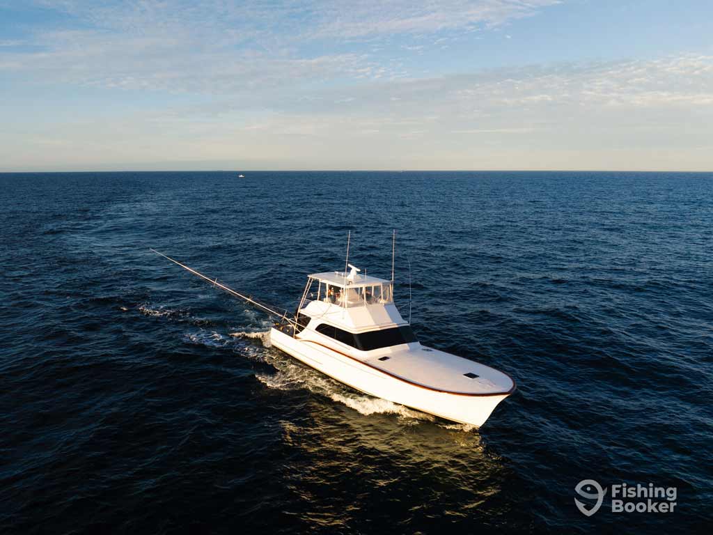 A white sportfishing boat’s gliding across calm waters under a partly cloudy sky—ideal for the Virginia Beach Billfish Tournament. The Fishing Booker logo’s in the bottom right corner.