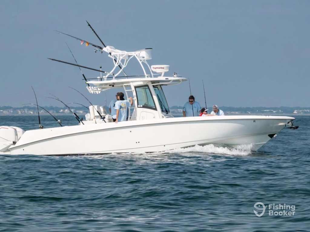 Four anglers fishing on a white sportfishing charter boat with several rods cruise across calm water during their deep sea fishing trip