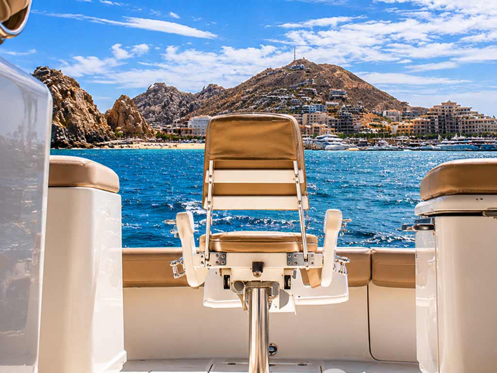 A view from a boat toward a coastal city with hills, blue sky, and clouds. The captain’s chair is ready for Bisbees Black and Blue action, right in the foreground.