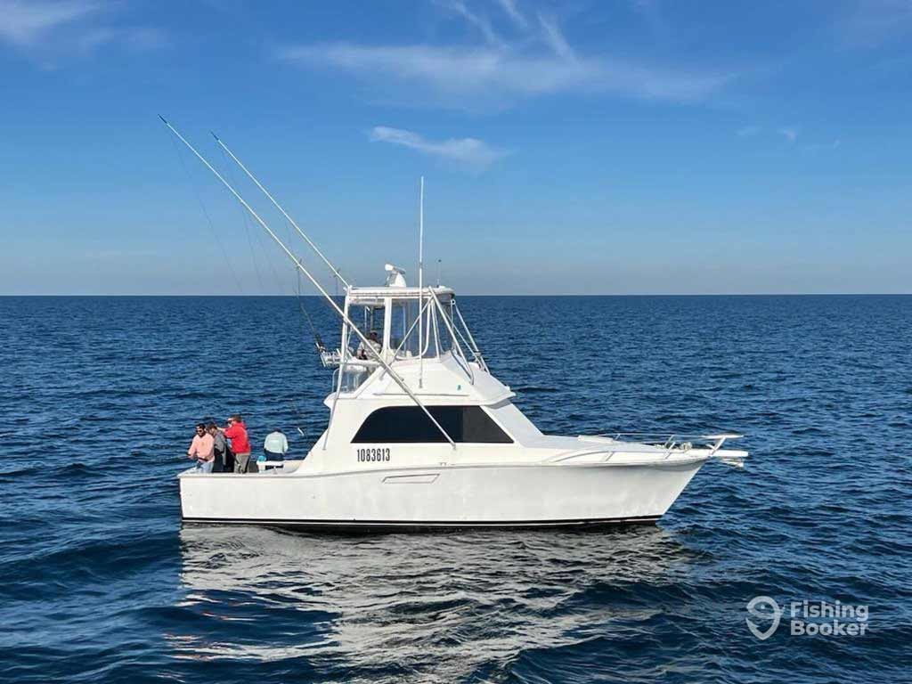 A white sportfishing boat with three anglers floats on calm water under a clear sky, likely headed to the Blue Marlin Grand Championship.